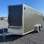 a black and silver trailer is parked in a gravel lot .