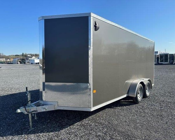 a black and silver trailer is parked in a gravel lot .