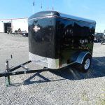 a black trailer is parked in a gravel lot in front of a building .
