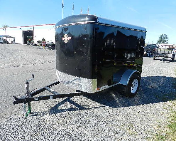 a black trailer is parked in a gravel lot in front of a building .