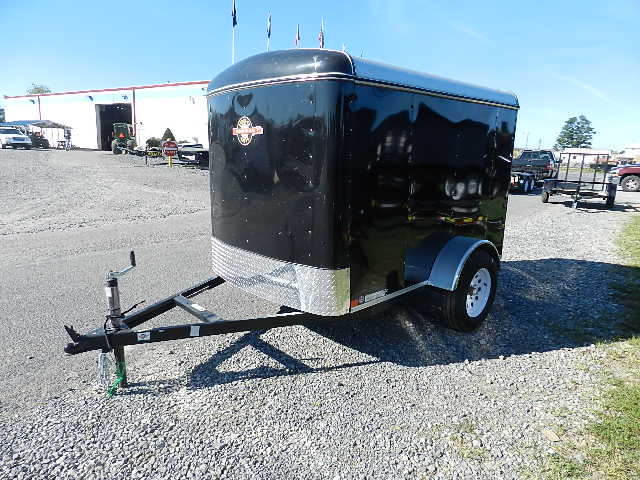 a black trailer is parked in a gravel lot in front of a building .