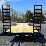 a trailer with a wooden deck is parked in a gravel lot .