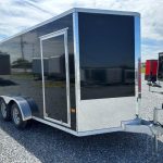 a black and silver trailer is parked in a gravel lot