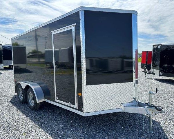 a black and silver trailer is parked in a gravel lot