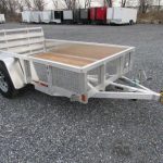 a small aluminum trailer with a wooden deck is parked in a gravel lot .
