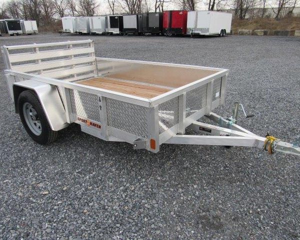 a small aluminum trailer with a wooden deck is parked in a gravel lot .