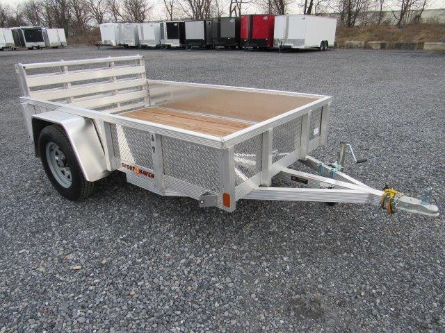 a small aluminum trailer with a wooden deck is parked in a gravel lot .