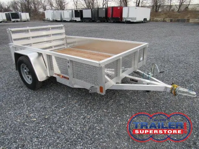 a small aluminum trailer with a wooden deck is parked in a gravel lot .