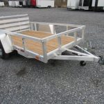 a small Sport Haven aluminum trailer with a wooden deck parked in a gravel lot