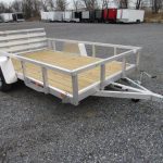 a small aluminum trailer with a wooden deck is parked on a gravel lot