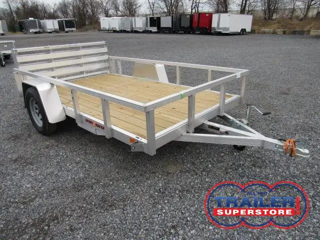 a small aluminum trailer with a wooden deck is parked on a gravel lot