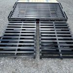 a black metal ramp attached to a trailer is sitting on top of a gravel road
