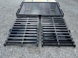 a black metal ramp attached to a trailer is sitting on top of a gravel road