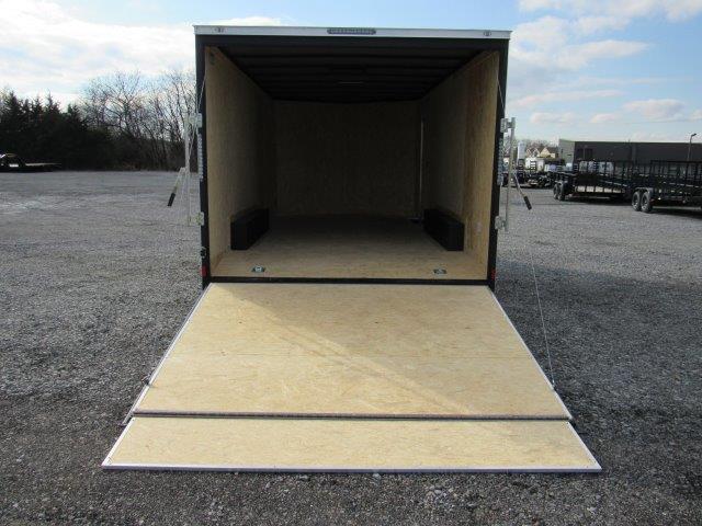 a covered wagon trailer with the door open is sitting in a parking lot .