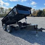a black dump trailer parked in a gravel lot
