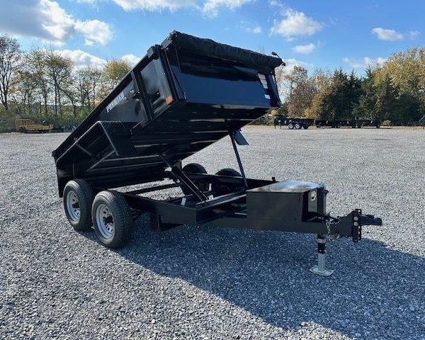 a black dump trailer parked in a gravel lot