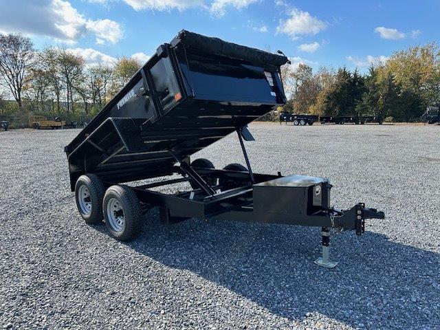 a black dump trailer parked in a gravel lot