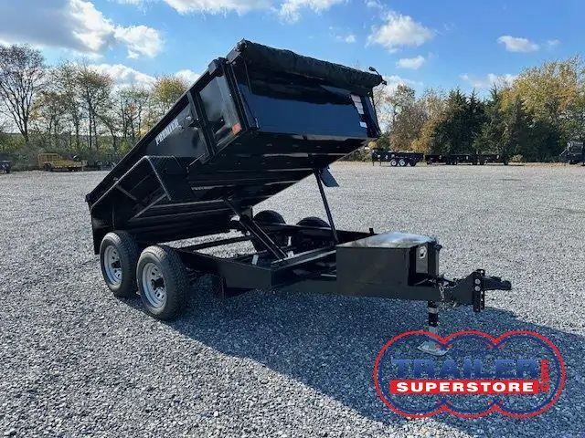 a black dump trailer parked in a gravel lot