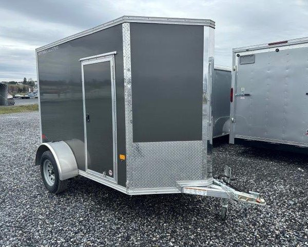 a black and silver trailer is parked in a gravel lot