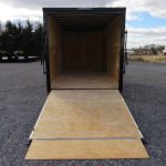 an empty trailer with a wooden ramp is parked in a gravel lot .