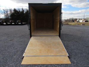an empty trailer with a wooden ramp is parked in a gravel lot .