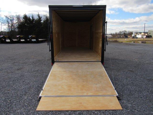 an empty trailer with a wooden ramp is parked in a gravel lot .