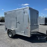 a gray trailer is parked in a gravel lot