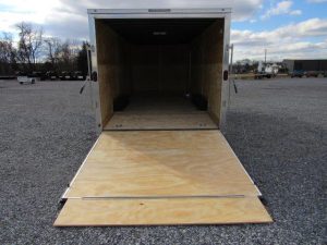 a trailer with a wooden floor is sitting in a gravel lot .