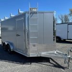 a silver trailer with a ladder on top of it is parked in a gravel lot .