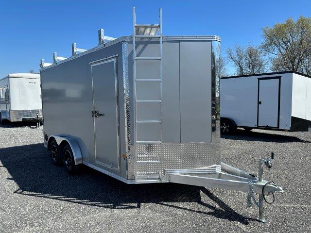 a silver trailer with a ladder on top of it is parked in a gravel lot .
