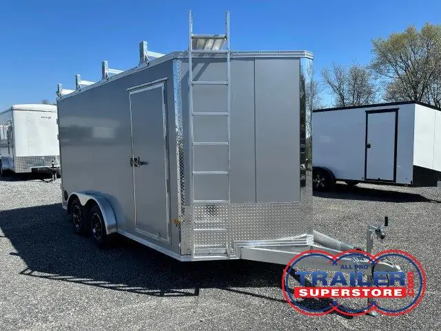 a silver trailer with a ladder on top of it is parked in a gravel lot .