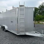 a silver trailer with a ladder attached to it is parked in a gravel lot .