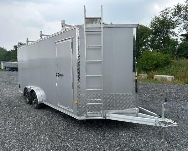 a silver trailer with a ladder attached to it is parked in a gravel lot .