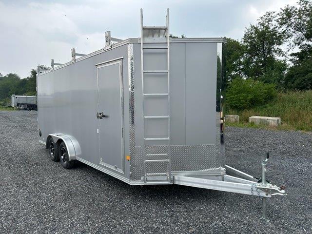 a silver trailer with a ladder attached to it is parked in a gravel lot .