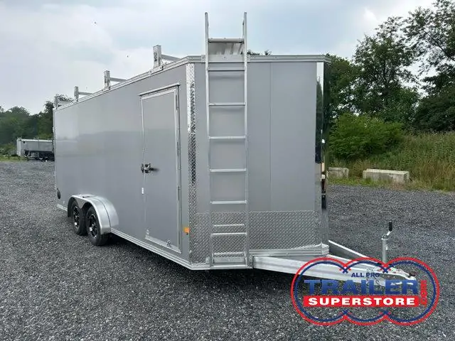 a silver trailer with a ladder attached to it is parked in a gravel lot .