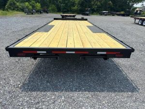 a flatbed trailer with a wooden deck is parked in a gravel lot .