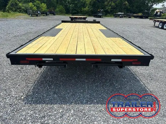 a flatbed trailer with a wooden deck is parked in a gravel lot .