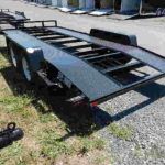 a black trailer parked in the grass on a gravel road