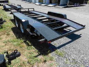 a black trailer parked in the grass on a gravel road