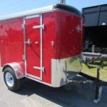 a red trailer is parked on the side of the road next to a dump trailer