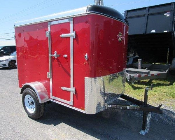 a red trailer is parked on the side of the road next to a dump trailer