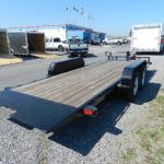 a trailer with a wooden deck is parked in a gravel lot