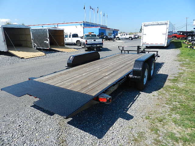 a trailer with a wooden deck is parked in a gravel lot