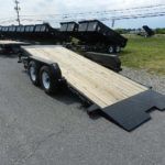 a black trailer with a wooden deck is parked on the side of the road .