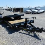 a black trailer with a wooden deck parked in a gravel lot
