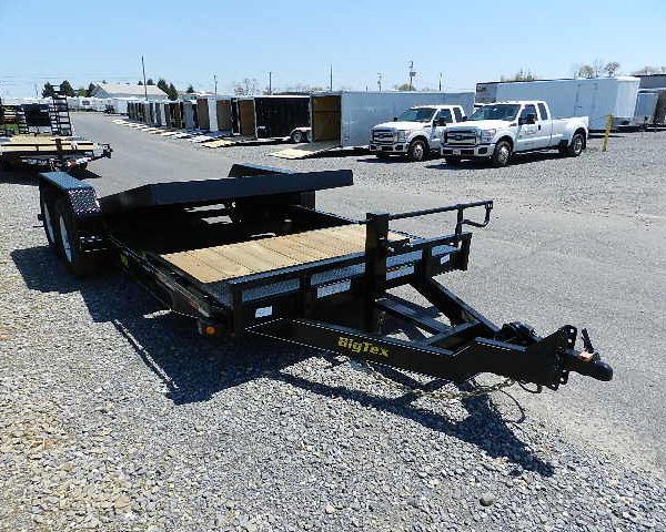 a black trailer with a wooden deck parked in a gravel lot