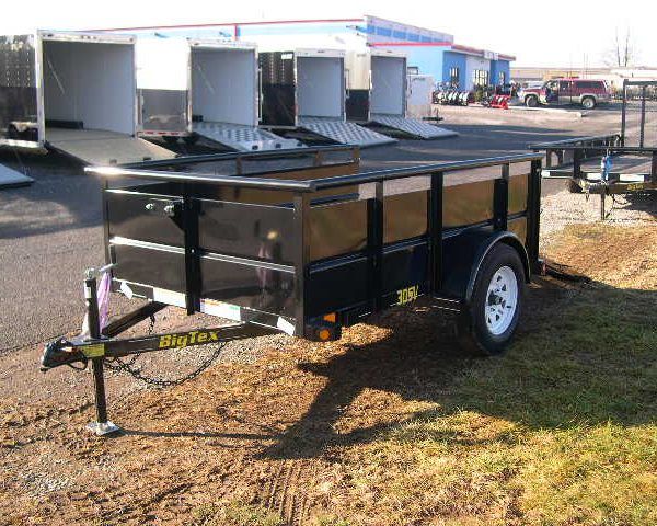 a black trailer is parked in the grass in front of a building .