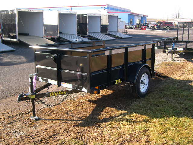 a black trailer is parked in the grass in front of a building .