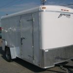 a white Homesteader cargo trailer is parked in a gravel lot