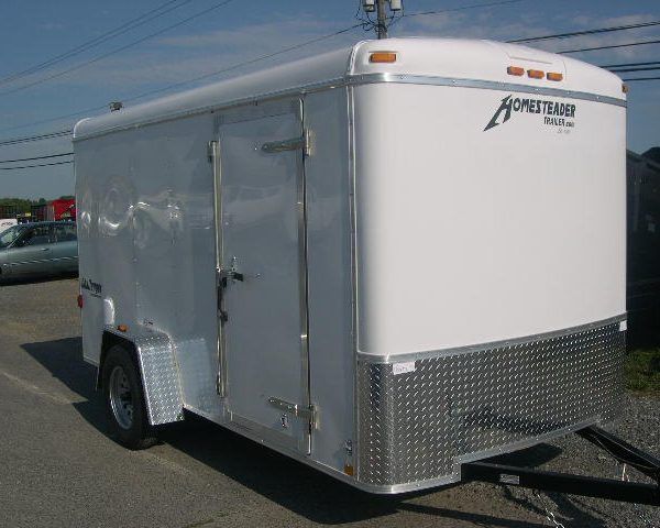 a white Homesteader cargo trailer is parked in a gravel lot
